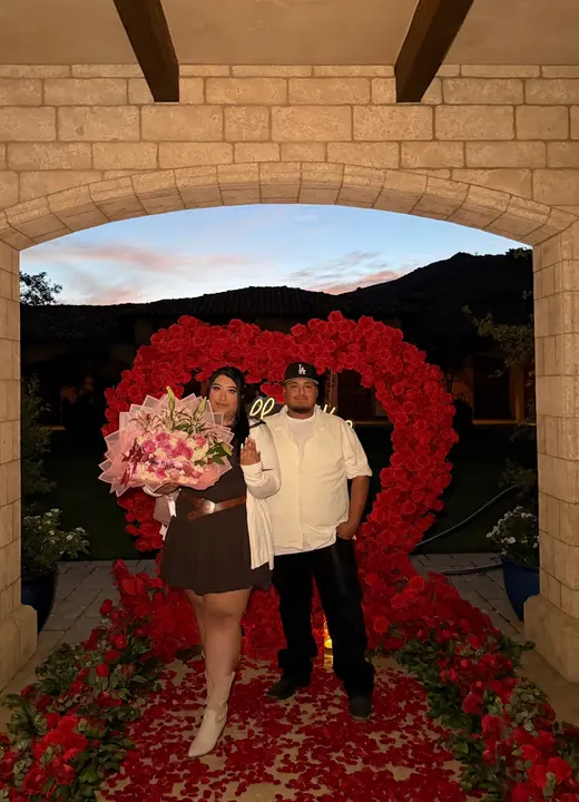 Newly engaged couple with red floral heart arch by Big Moments Co.