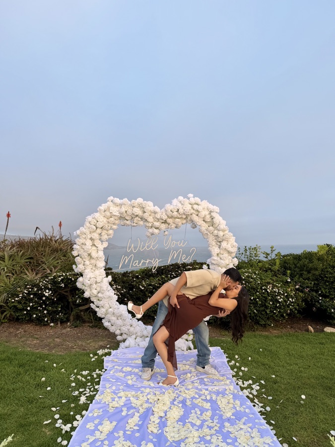 Couple posing with white floral heart arch by Big Moments Co.